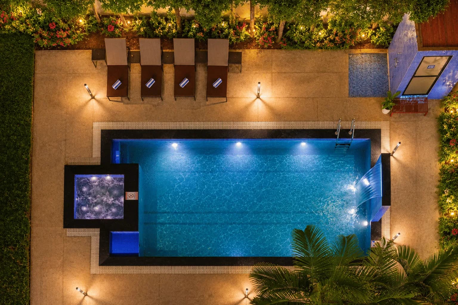 Illuminated resort pool surrounded by tropical planting at Summit Calangute